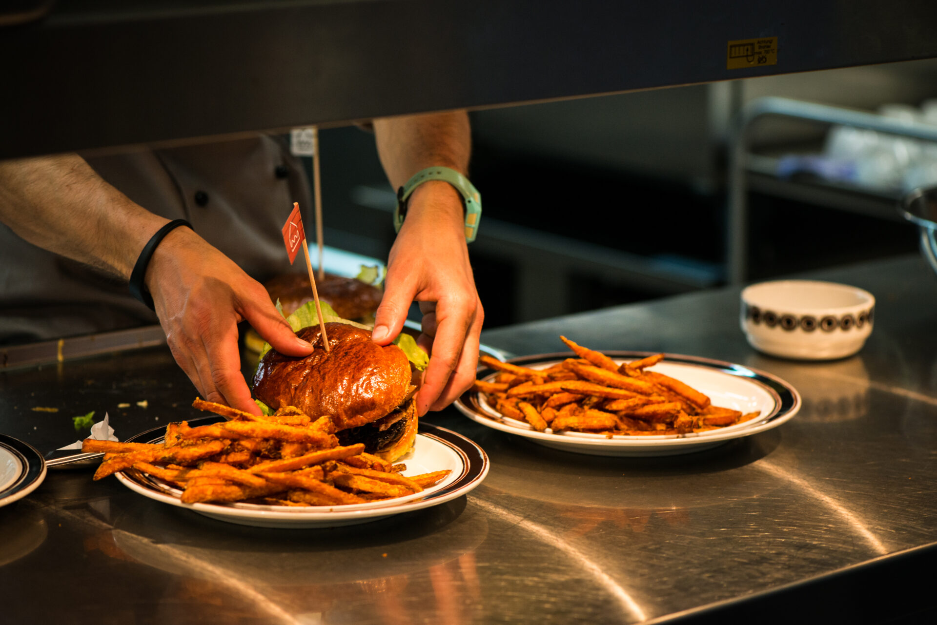 Zwei Hände richten einen Burger in der Seehaus Küche an. Als Beilage: Süßkartoffelpommes