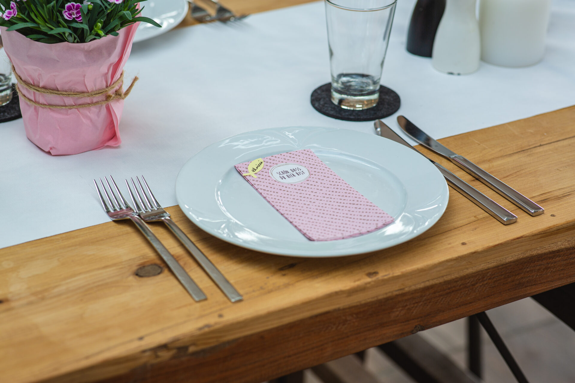 Eingedeckter Tisch mit weißem Porzellan Teller und rosa Serviette mit der Aufschrift 