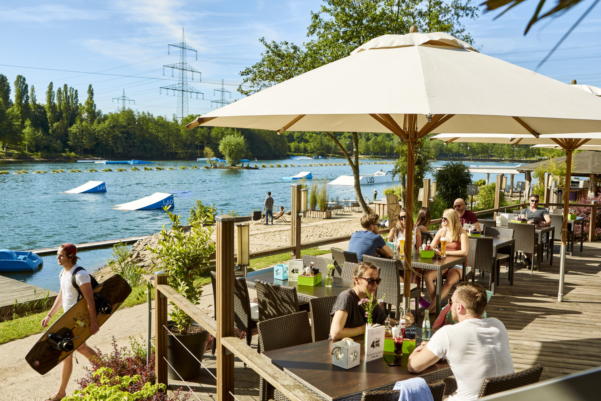 Blick auf das Treiben auf der sommerlichen Seehaus Terrasse. Im Hintergrund der See der Wasserskianlage