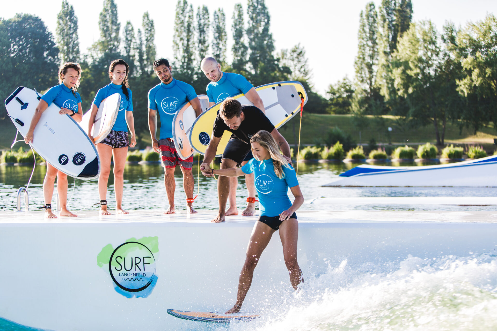 surf-langenfeld-anfänger-kurs-sommer Anfängerszene auf der Welle: Coach hilft Surferin beim ersten Start in die Welle