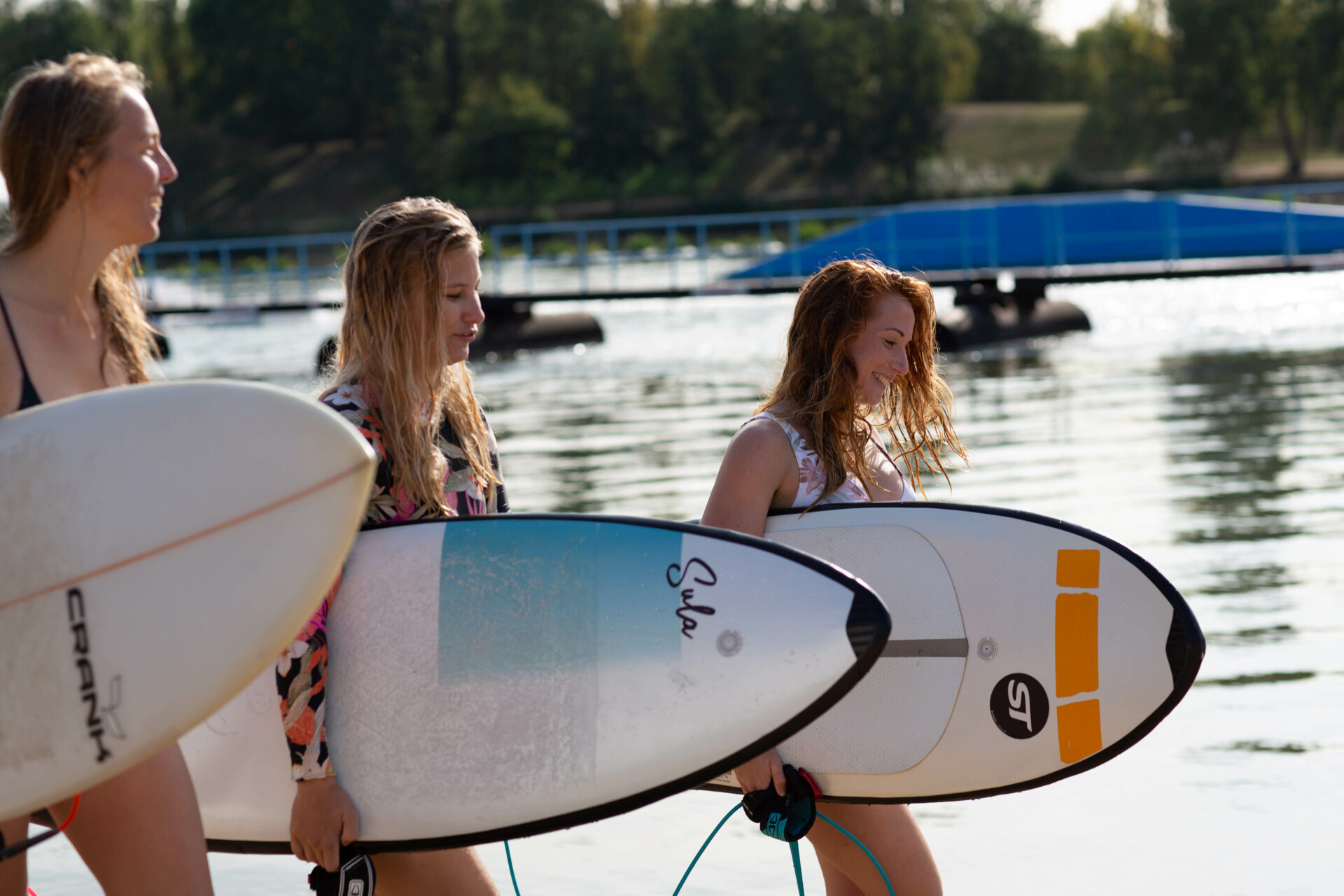 Drei Frauen in Badekleidung laufen mit Surfboards unter dem Arm am Stand entlang