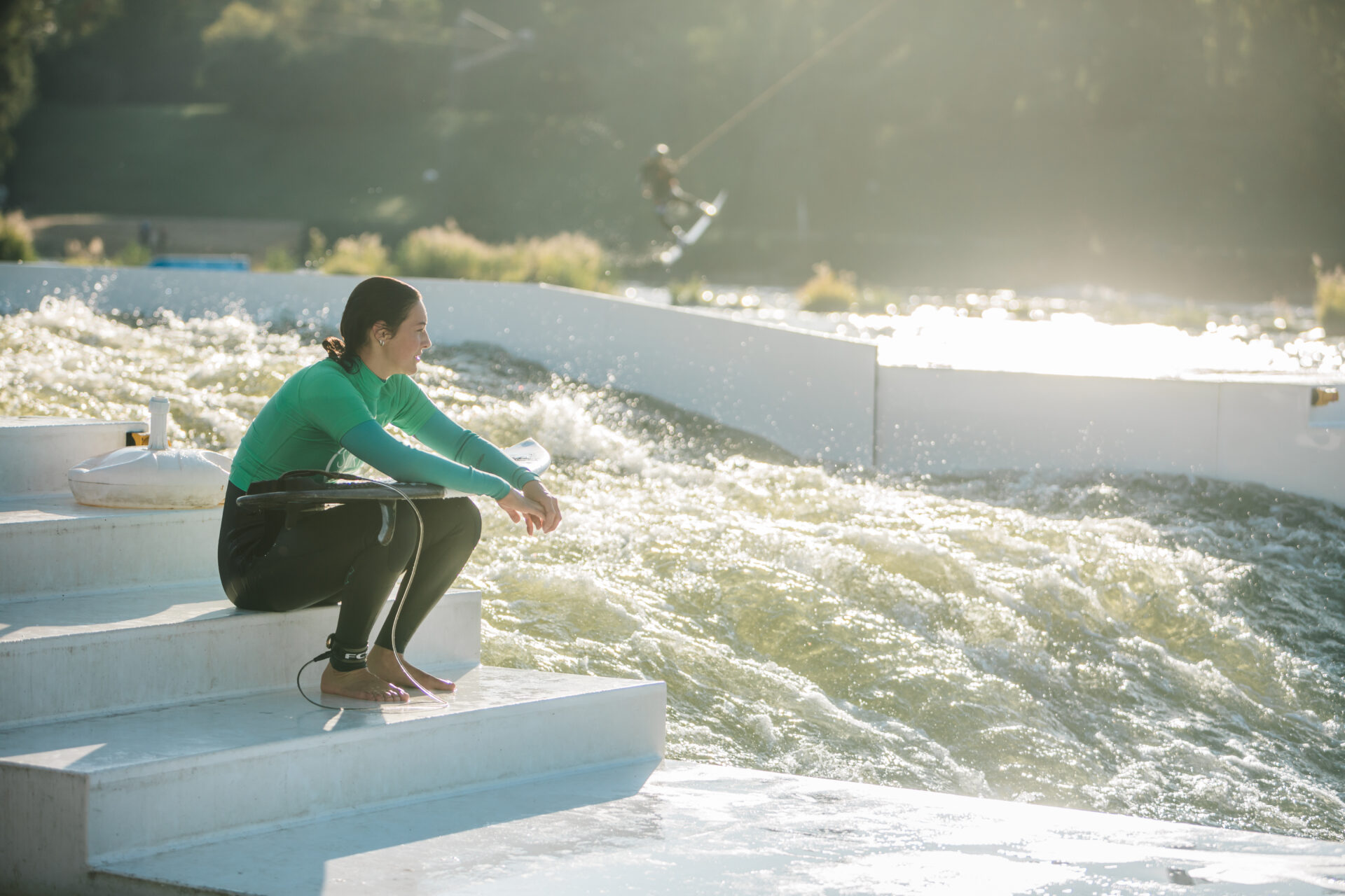 Surferin sitzt auf den Stufen der stehenden Welle, mit dem Surfboard auf dem Schoß und schaut in die Ferne