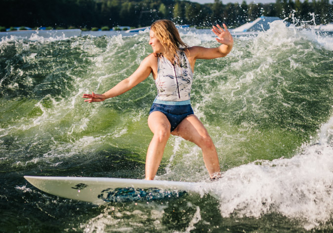 Eine blonde Frau surft im Sommer im Badeanzug auf der Surf Langenfeld Welle